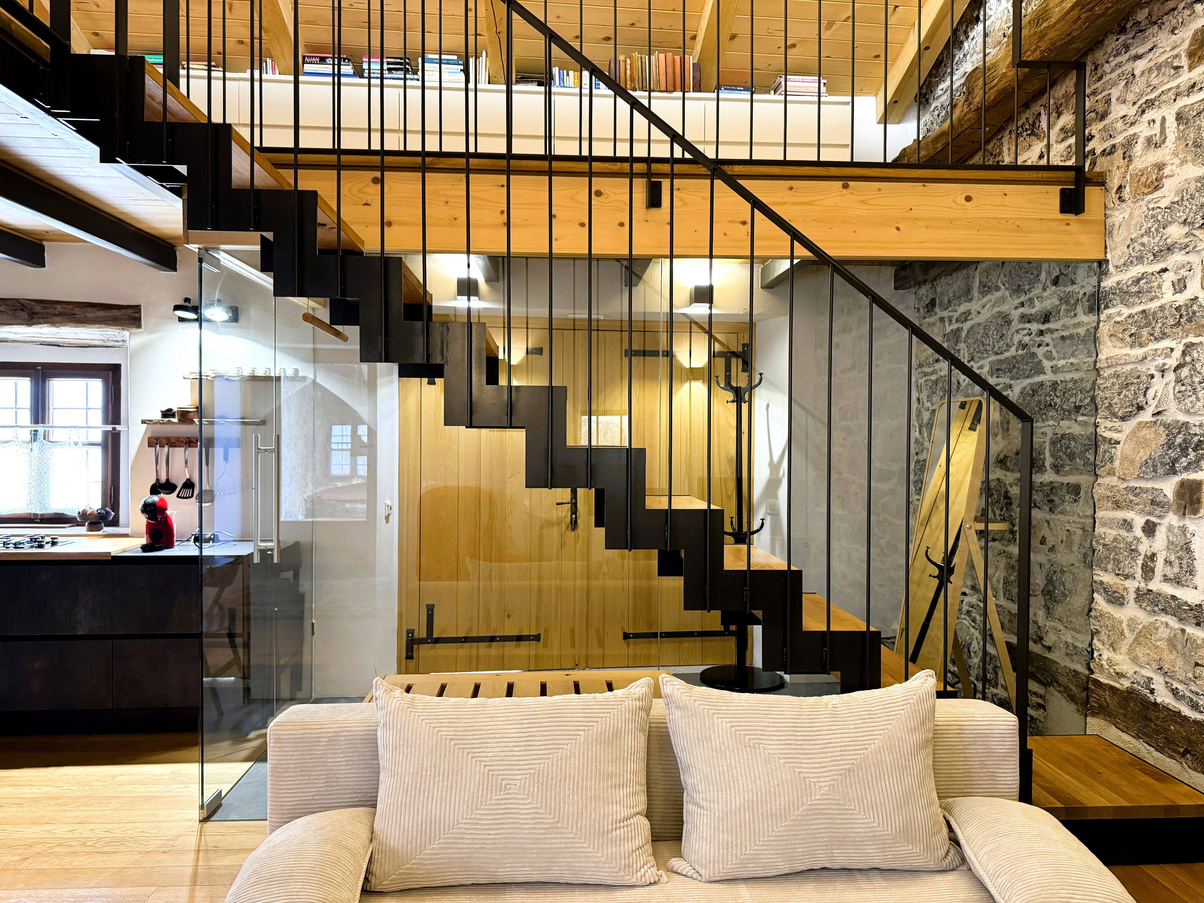 Un interior moderno con una escalera, una zona de cocina y un espacio de descanso con cojines.
