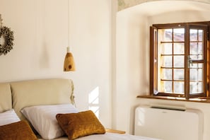 Quarto com cama, almofadas, luminária pendente, janela com vista e radiador.