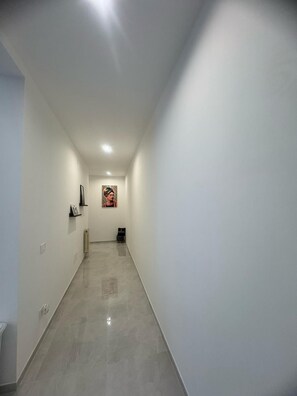 A narrow hallway with a tiled floor, white walls, and a single framed picture on the wall.