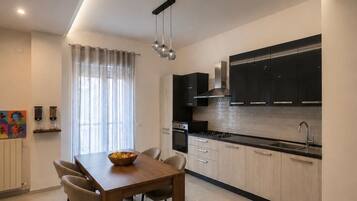 A modern kitchen with a dining area, featuring a wooden table, chairs, and a bowl of fruit.