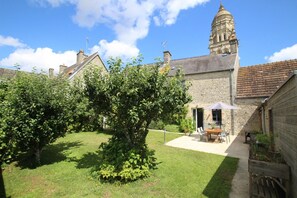 A courtyard with a stone building, a tree, and a table with chairs. - Cottage 'Gite Le Sainte Marie' with Private Terrace, Private Garden and Wi-Fi (Sainte-Marie-du-Mont)