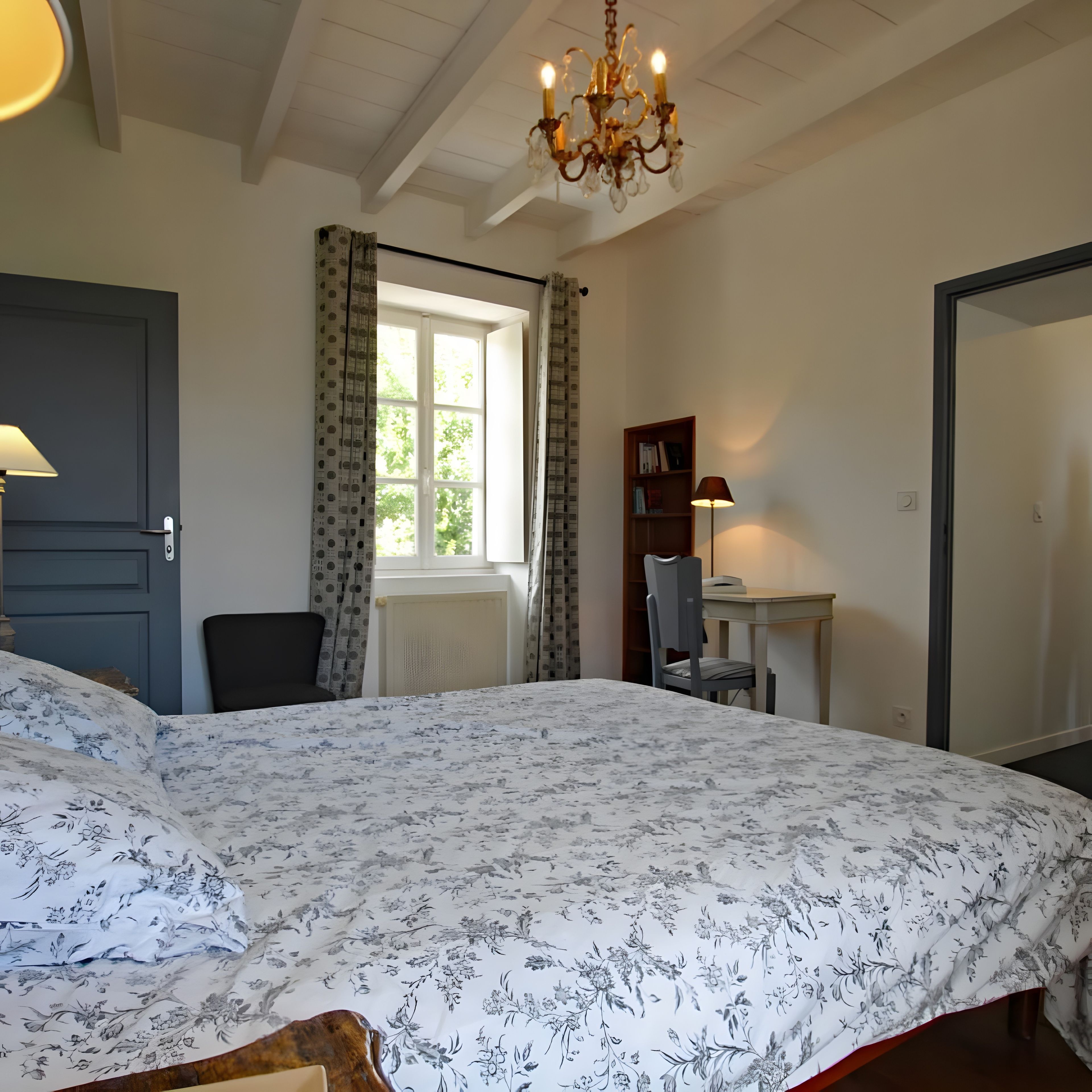 A bedroom with a bed, a desk, a chair, a bookshelf, and a chandelier.
