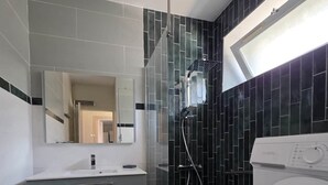 A modern bathroom with a glass shower enclosure, a built-in washing machine, and a vanity with a mirror.