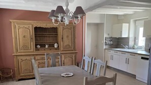 A dining area with a table and chairs, a wooden cabinet with shelves, and a kitchen area with cabinets and a sink.