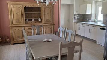 Ein Essbereich mit Tisch und Stühlen, eine Holzkommode mit Regalen sowie eine Küchenzeile mit Schränken und Spüle.