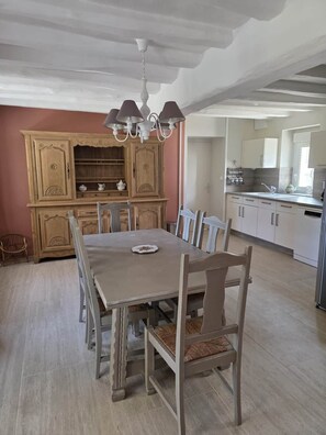 A dining area with a table and chairs, a wooden cabinet with shelves, and a kitchen area with cabinets and a sink.