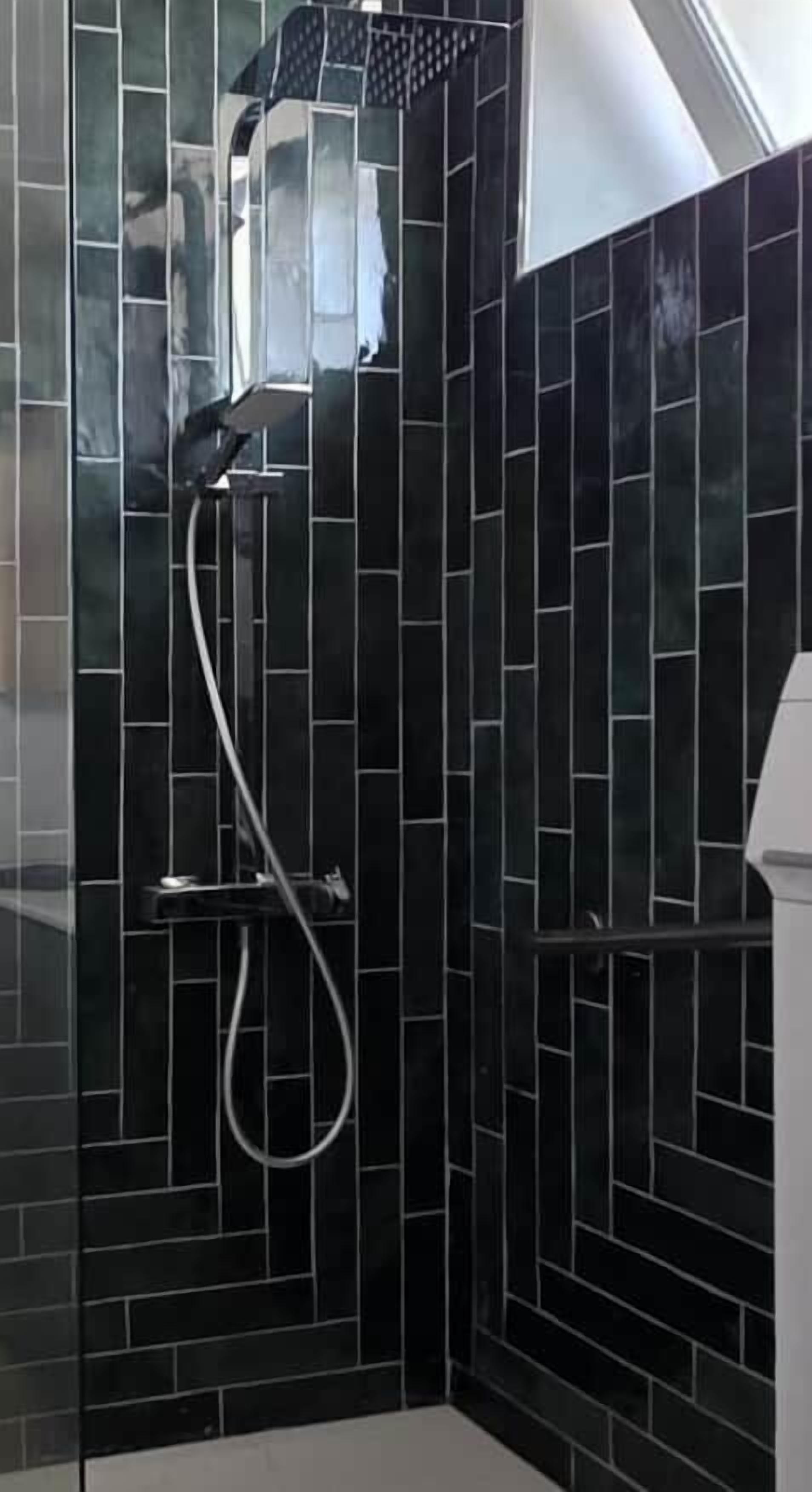 Een douchegedeelte met zwarte betegelde wanden en een handdouche.