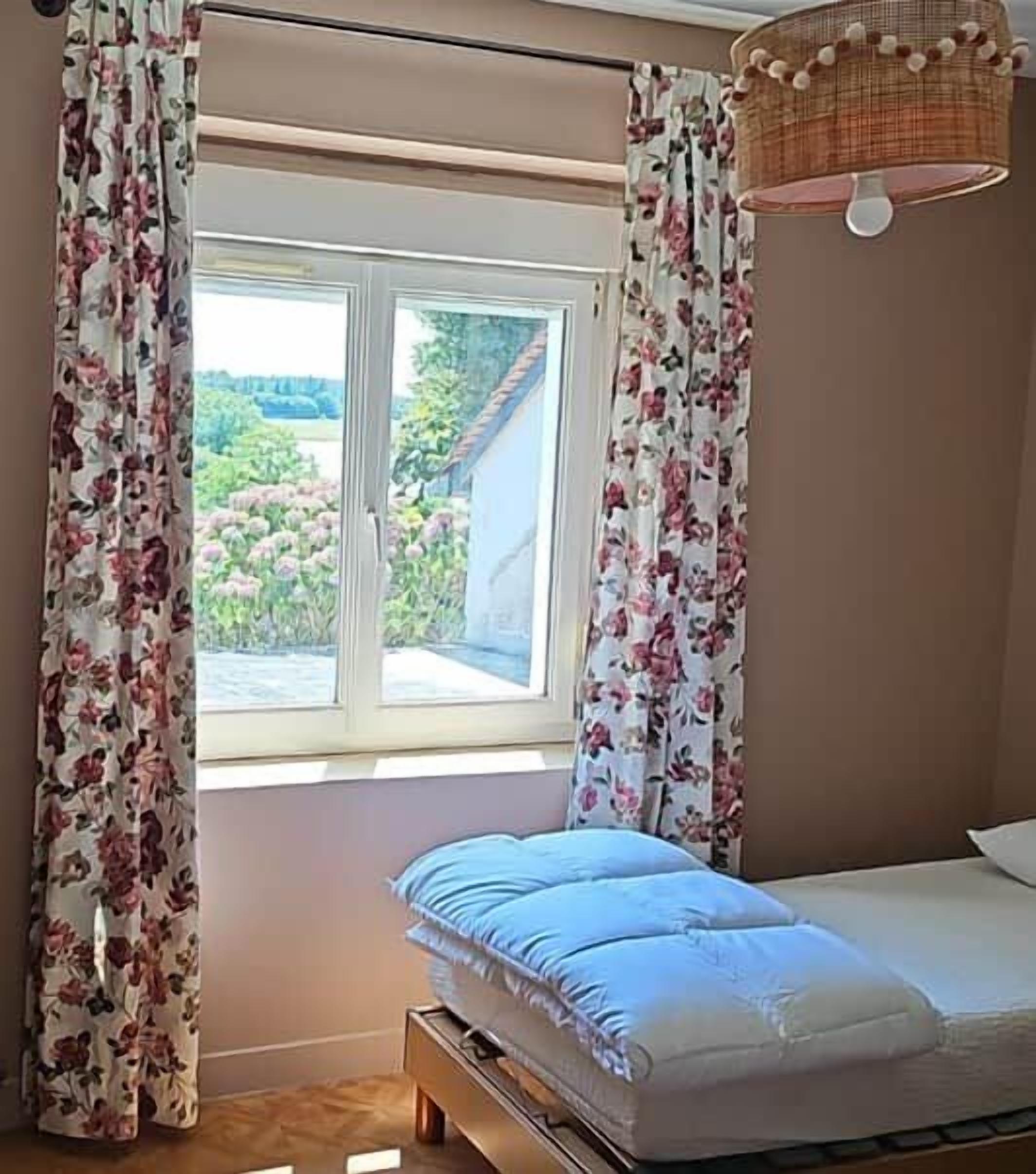 Ein Schlafzimmer mit Bett, einem Fenster mit Vorhängen und einer Pendelleuchte.