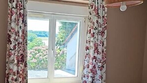 A bedroom with a bed, a window with curtains, and a hanging lamp.