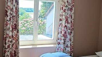 Ein Schlafzimmer mit Bett, einem Fenster mit Vorhängen und einer Pendelleuchte.