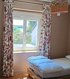 A bedroom with a bed, a window with curtains, and a hanging lamp.