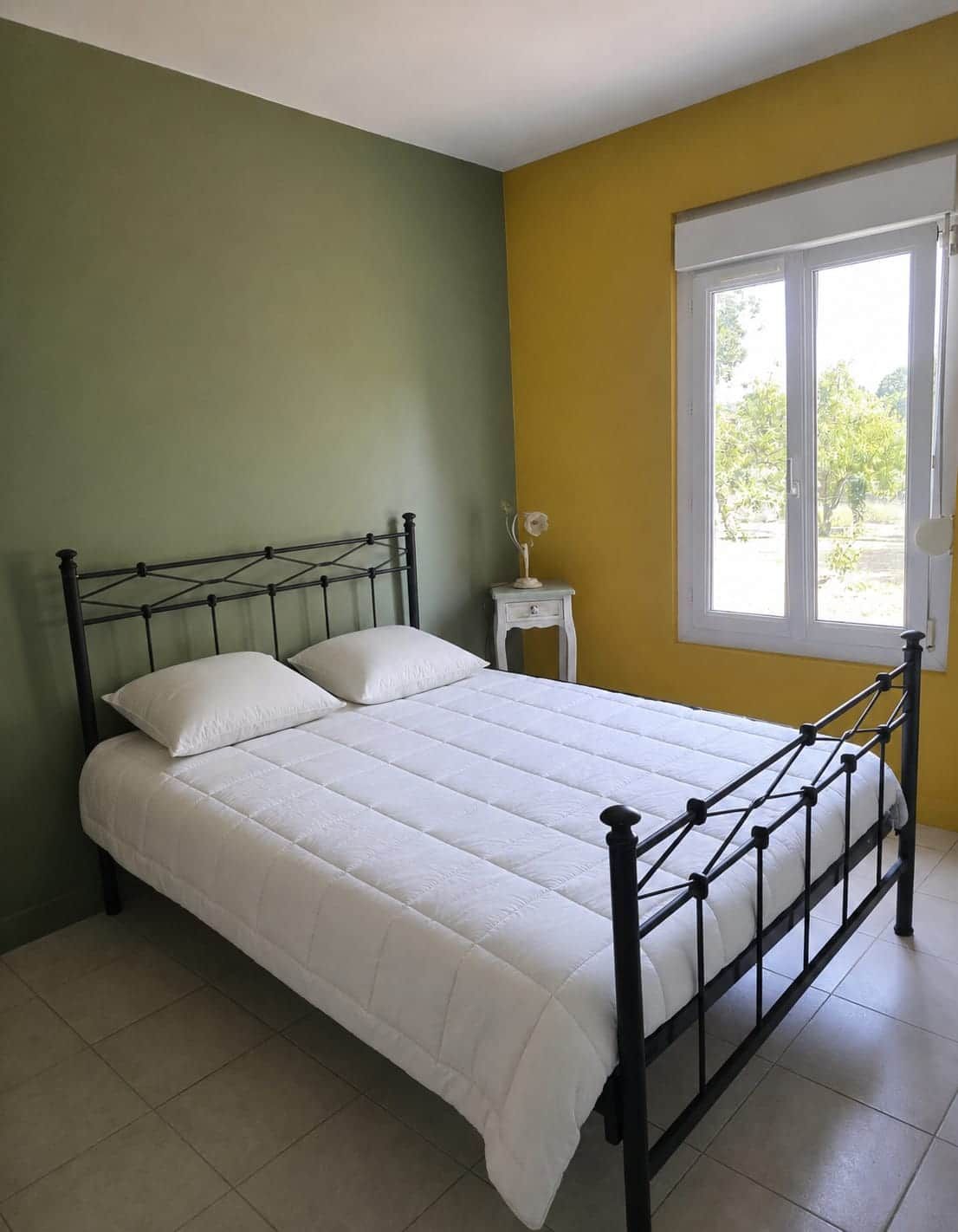 Una cama individual con estructura metálica, ropa de cama blanca y una mesita de noche con lámpara.