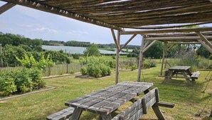 An outdoor picnic area with wooden tables and benches, surrounded by a grassy lawn and a wooden fence.