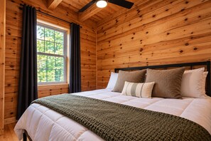 A wooden-paneled bedroom with a bed, a window with curtains, and a ceiling fan. - Abode at Big Pine – Formerly Western Hideaway (Logan)