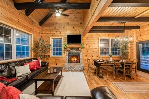 A cozy cabin interior with a fireplace, wooden walls, a leather sofa, and a dining area. - Abode at Big Pine – Formerly Western Hideaway (Logan)