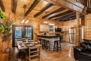 A wooden cabin interior with a dining area, kitchen, and a stone island. - Abode at Big Pine – Formerly Western Hideaway (Logan)