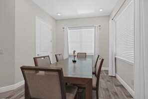 A dining room with a rectangular table, six chairs, white curtains, and a ceiling light fixture. - Pickled Parrot Cottage - Private Pool Near Disney & Island H2O Access - 8024ST (Kissimmee)