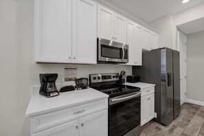 A modern kitchen with white cabinetry, a stainless steel microwave, a black stove, and a large refrigerator. - Pickled Parrot Cottage - Private Pool Near Disney & Island H2O Access - 8024ST (Kissimmee)