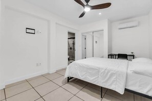 Ein Schlafzimmer mit einem Bett, einem Deckenventilator, einem Nachttisch und einer wandmontierten Klimaanlage.