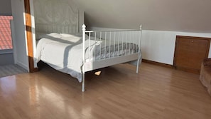 Ein Zimmer mit einem weißen Metallbett, Holzboden und einer Holztür.