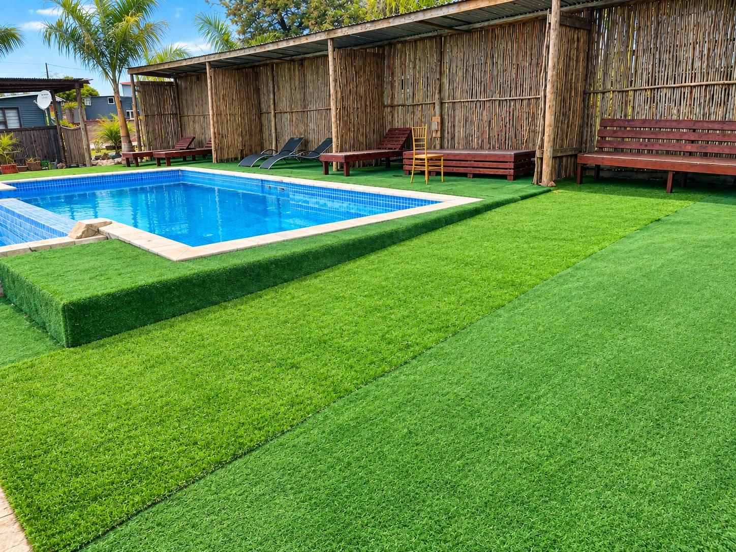 A swimming pool with artificial grass, wooden deck, and lounge chairs.