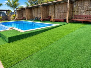 A swimming pool with artificial grass, wooden deck, and lounge chairs.