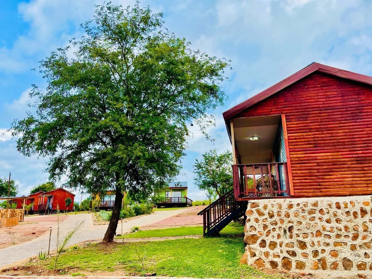 A red wooden building with a stone wall, a staircase, and a tree in front.