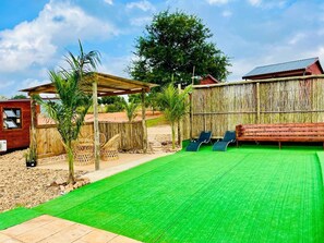 Un jardin avec une pelouse artificielle verte, une pergola en bois, une clôture en bambou et une terrasse en bois équipée de chaises longues.