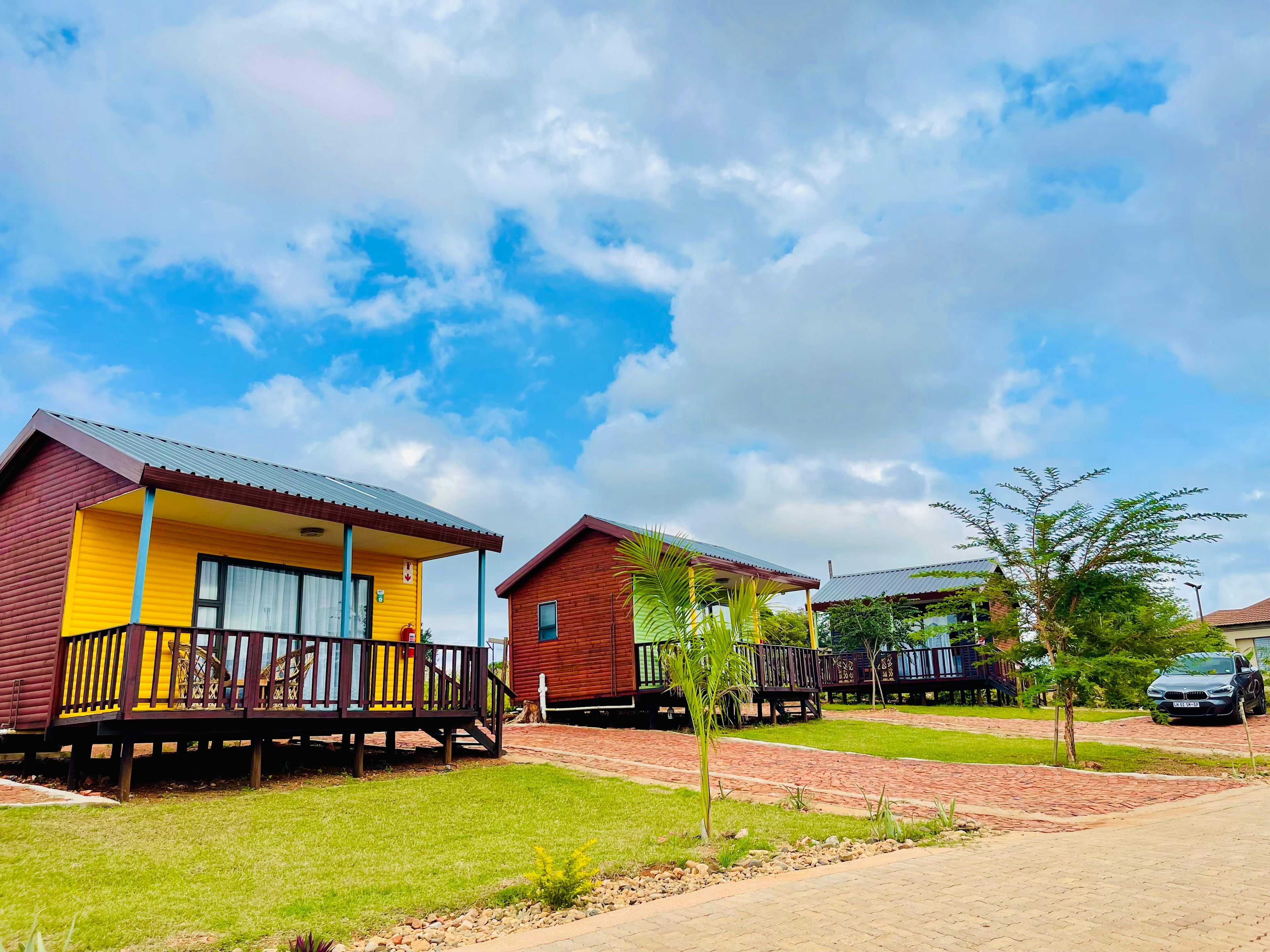 Two cabins with balconies, a paved walkway, and a car parked nearby.