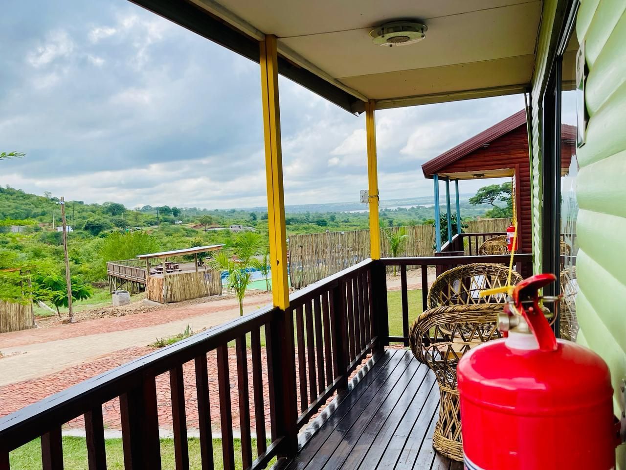 A covered porch with a view of a rural landscape, a red fire extinguisher, and a wicker chair.