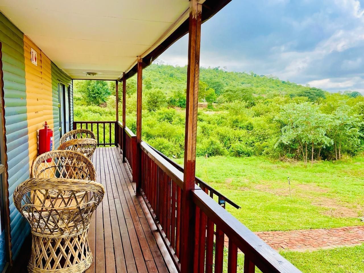 Eine überdachte Veranda mit Korbstühlen, einem Feuerlöscher und Blick auf eine grüne Landschaft.