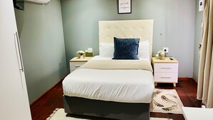 Une chambre à coucher comprenant un lit, des tables de chevet, un climatiseur fixé au mur, un cadre avec une citation et un tapis à motifs.
