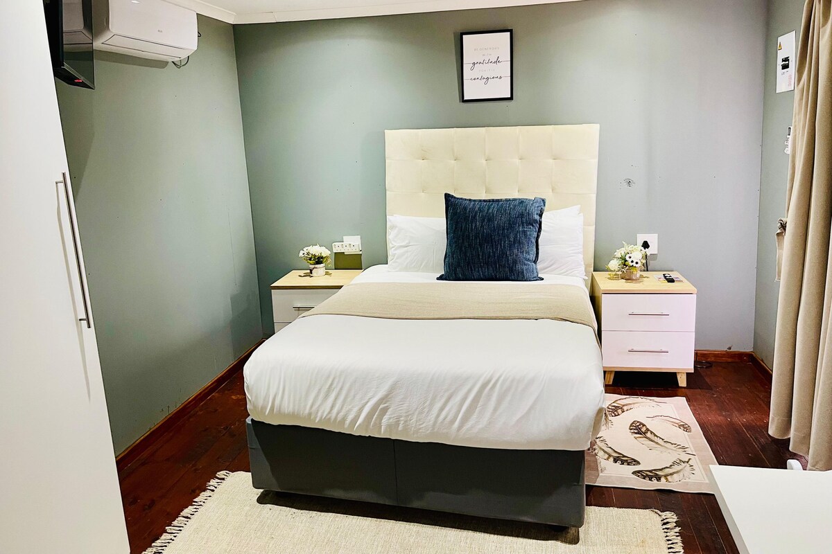 A bedroom with a bed, bedside tables, a wall-mounted air conditioner, a framed quote, and a patterned rug.