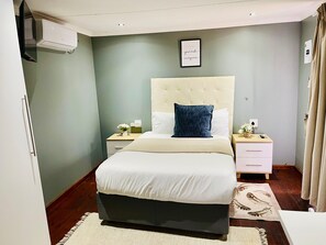 A bedroom with a bed, bedside tables, a wall-mounted air conditioner, a framed quote, and a patterned rug. - Damview Eco Lodge  (Thohoyandou)