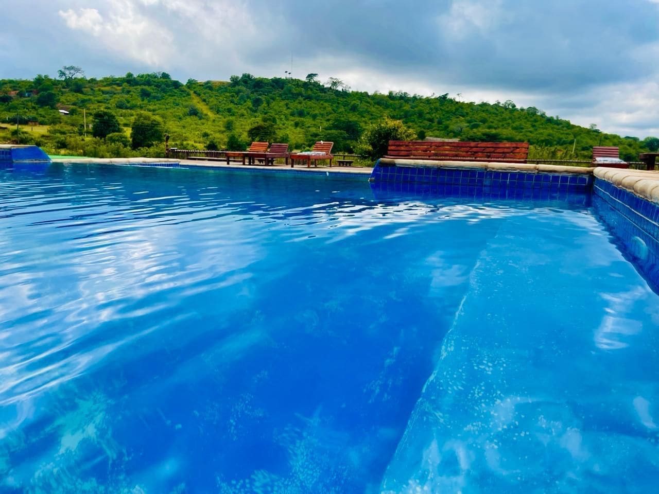 Una piscina con agua azul cristalina, rodeada por una terraza de madera con sillas de descanso.