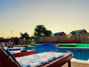 Un espace piscine comprenant plusieurs piscines, des chaises longues et une terrasse en bois.