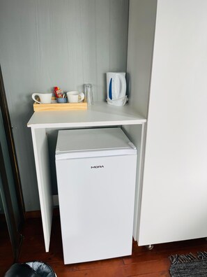 Une petite cuisine équipée avec un réfrigérateur blanc, une machine à café et un petit plan de travail sur lequel se trouvent une tasse et un livre.