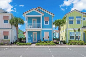 Une rangée de maisons colorées, avec une maison bleue au centre, dotée d’un balcon et d’une porte sur laquelle figure un numéro.