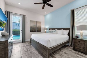 A bedroom with a bed, a nightstand, a lamp, a ceiling fan, and a view of a pool through the window. - Sun Shack Cottage | Private Pool Near Disney & Island H2O Access - 8096KD (Kissimmee)