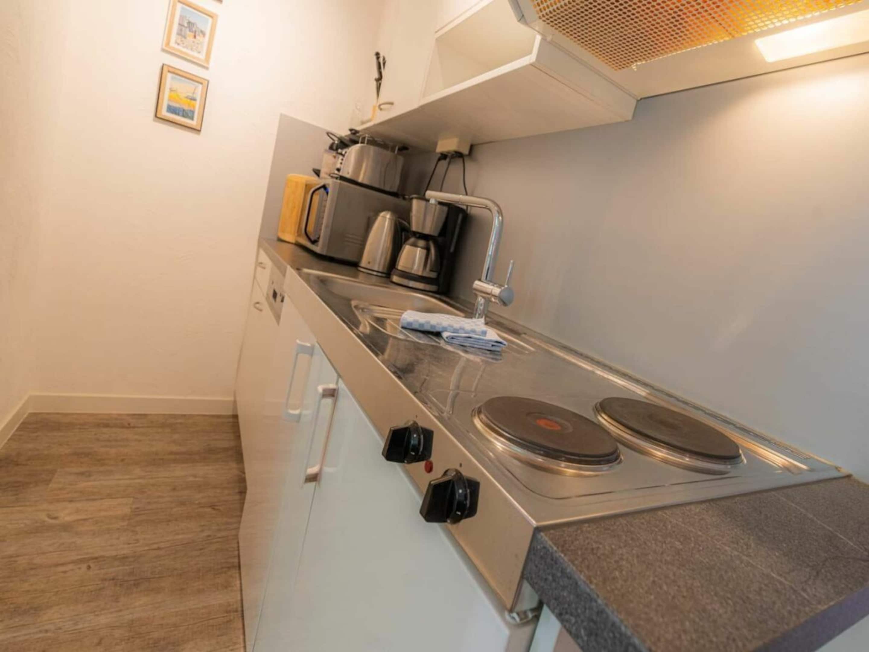 A compact kitchen with a built-in stove, a coffee maker, and a kettle.