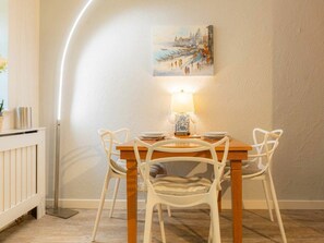 A dining area with a wooden table and white chairs, a painting on the wall, and a floor lamp. - "seenelke" (St. Peter-Ording)