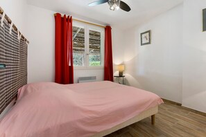 A bedroom with a bed, a window with curtains, a radiator, a lamp on a side table, and a ceiling fan. - Country House 'Mas Saint Joseph' with Private Pool, Private Terrace and Wi-Fi (Meynes)
