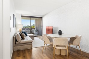 A modern living room with a sofa, a round dining table with chairs, a glass door leading to a balcony, and a 'GUEST READY' sign. - GuestReady-Luxurious Retreat with Rooftop Pool (Vila Nova de Gaia)