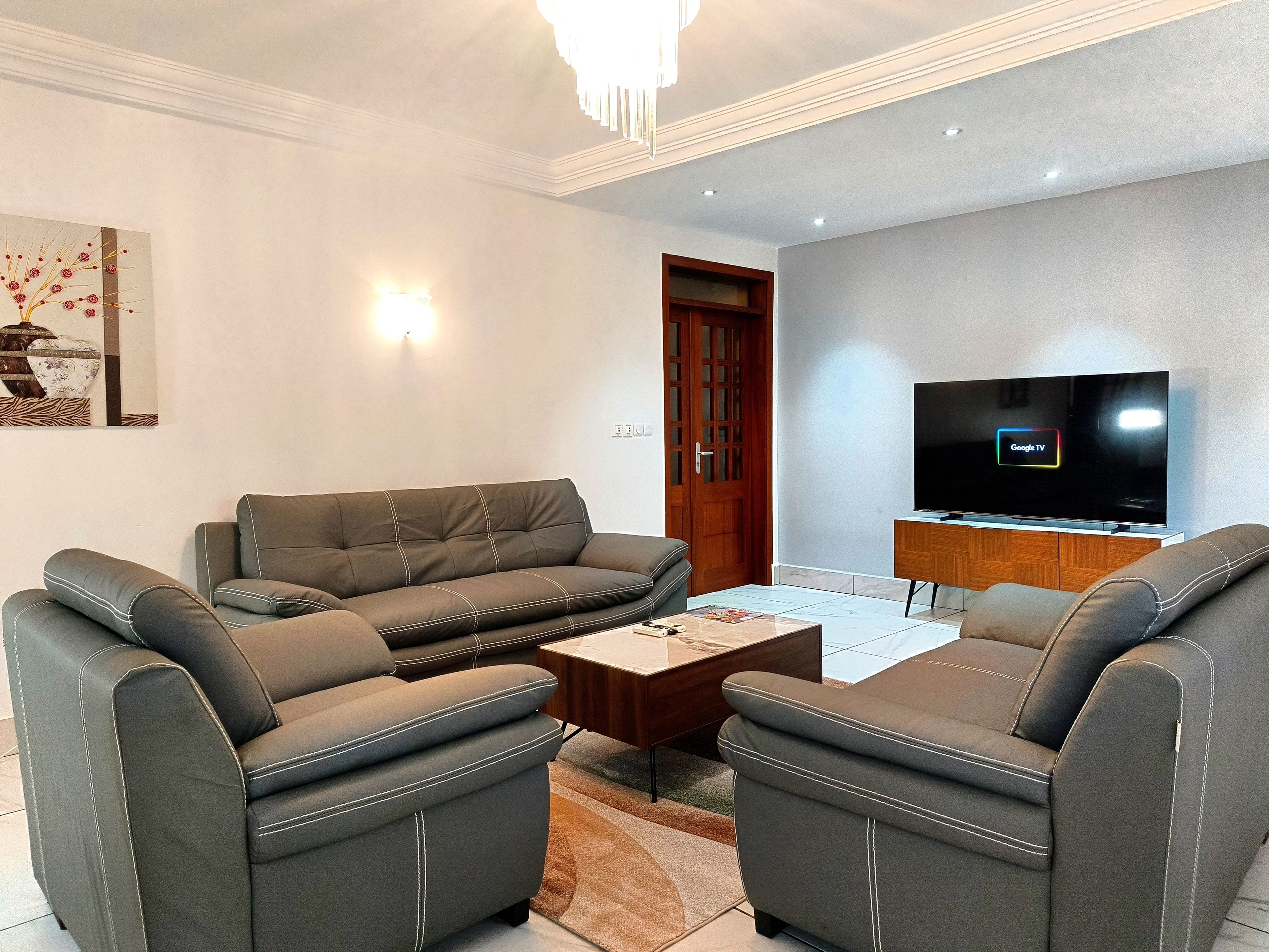 Ein modernes Wohnzimmer mit einer grauen Sofagarnitur, einem Couchtisch und einem flachbildfernseher an der Wand.