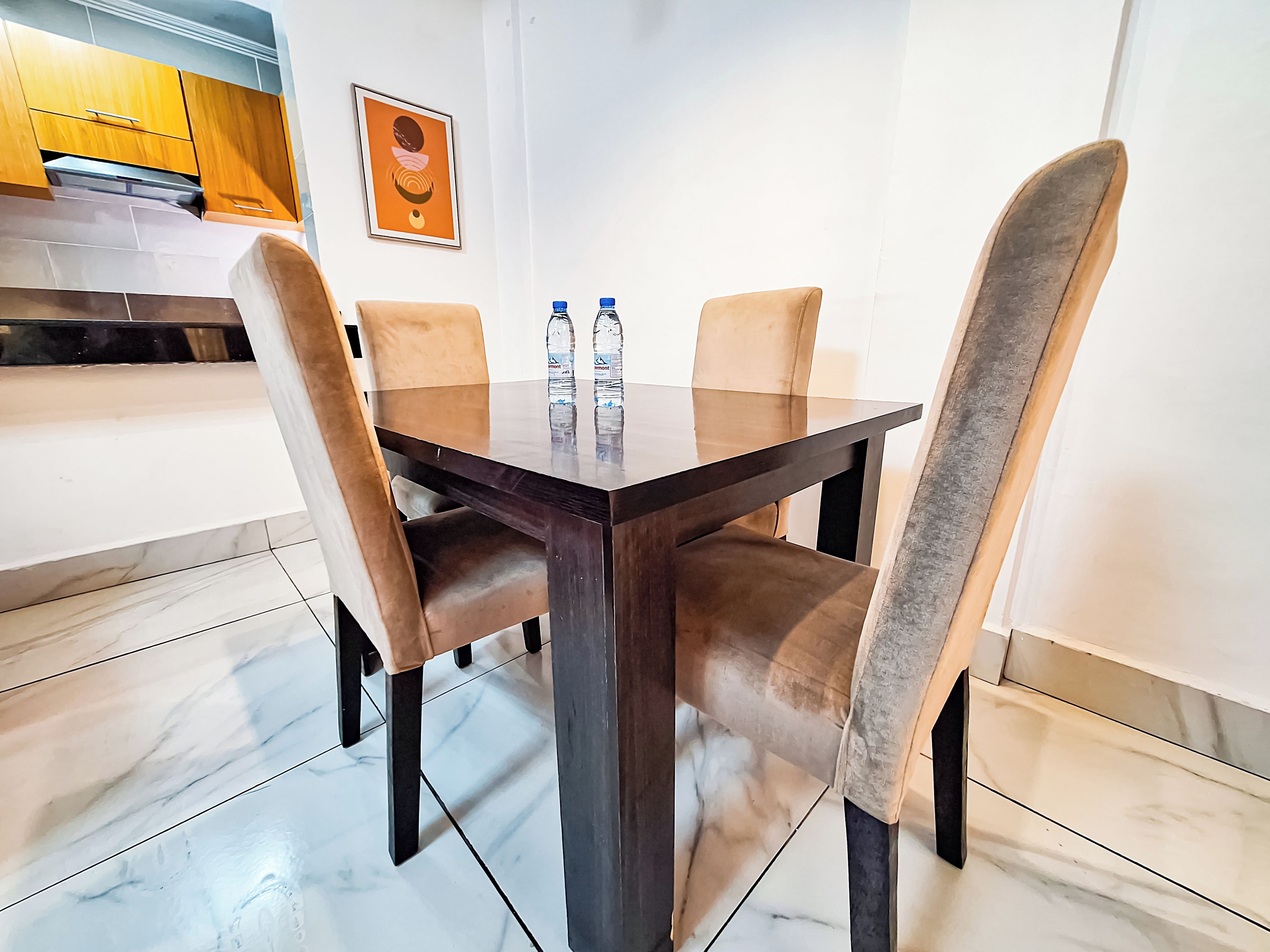 A dining table with four chairs, two bottles of water, and a framed picture on the wall.