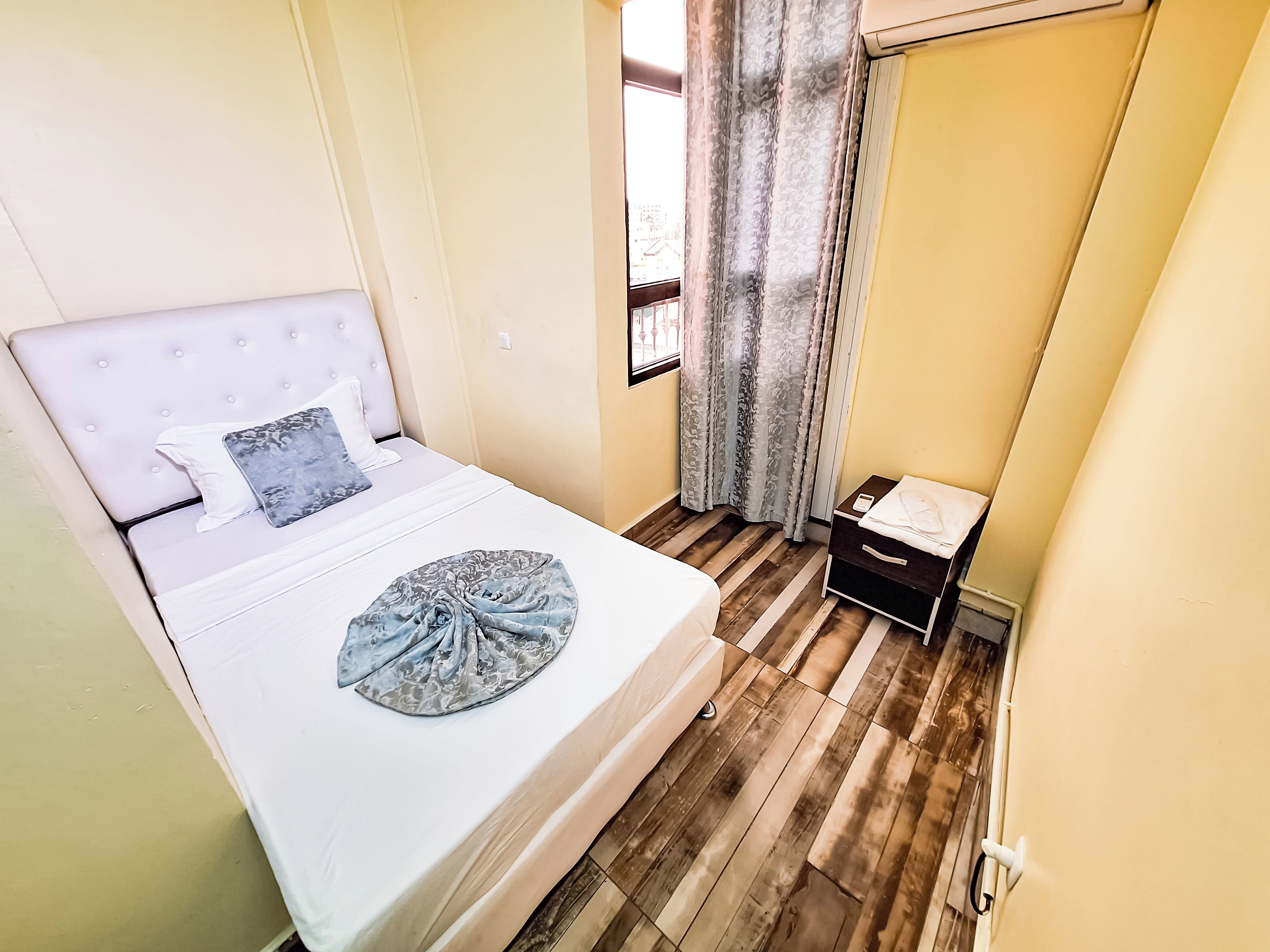 Una camera da letto con un letto, un comodino, una finestra con tende e un pavimento in legno.