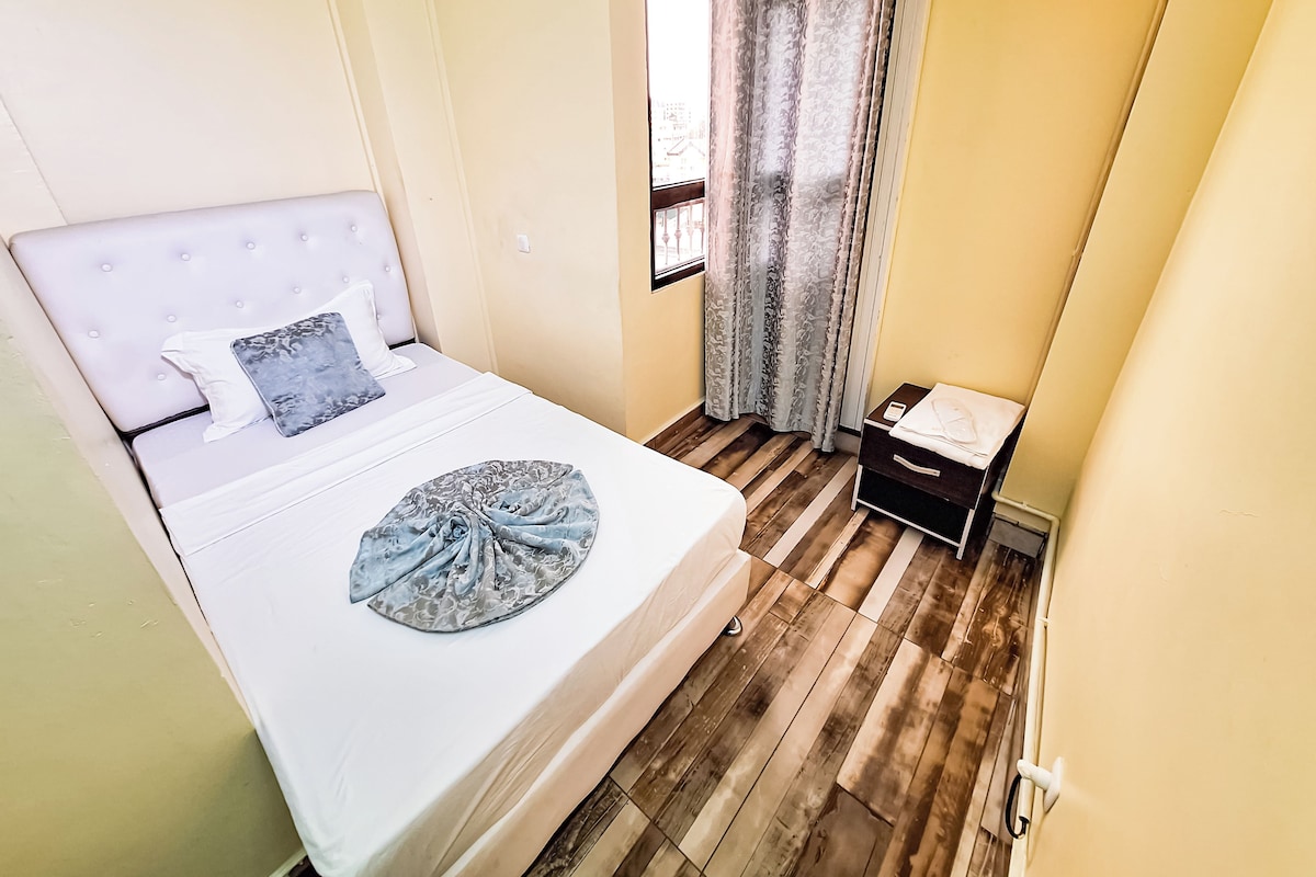 Een slaapkamer met een bed, nachtkastje, raam met gordijnen en een houten vloer.