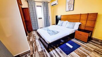 A hotel room with a bed, bedside table, nightstand, and a blue rug.