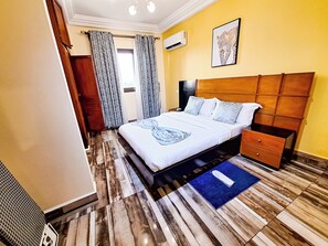 A hotel room with a bed, bedside table, nightstand, and a blue rug.