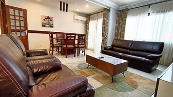 A living room with a brown leather sofa, a white coffee table, and a brown leather couch. There is a dining table with chairs in the background.
